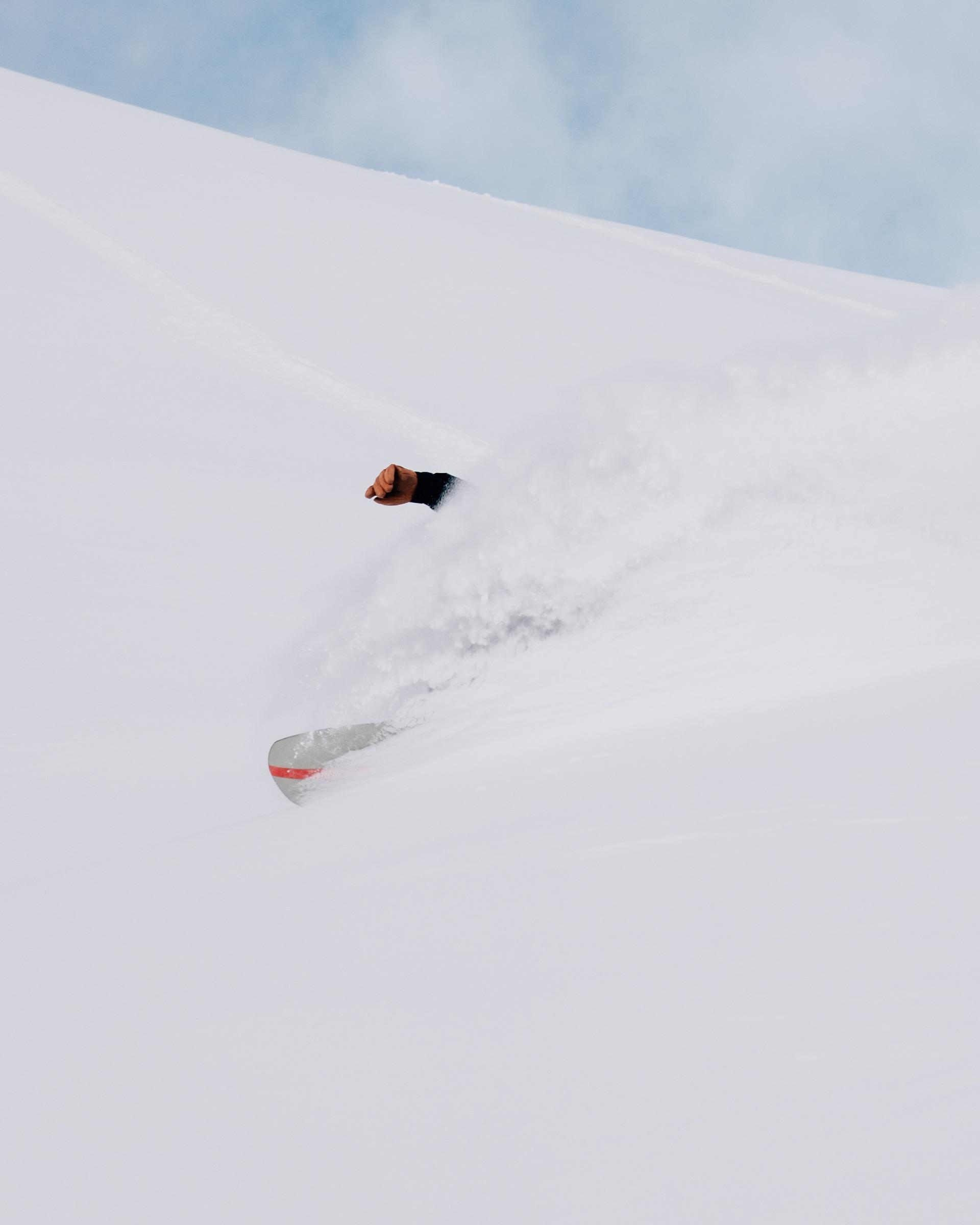 Snowboarder en pleine poudreuse, neige projetée sur une face de montagne suisse